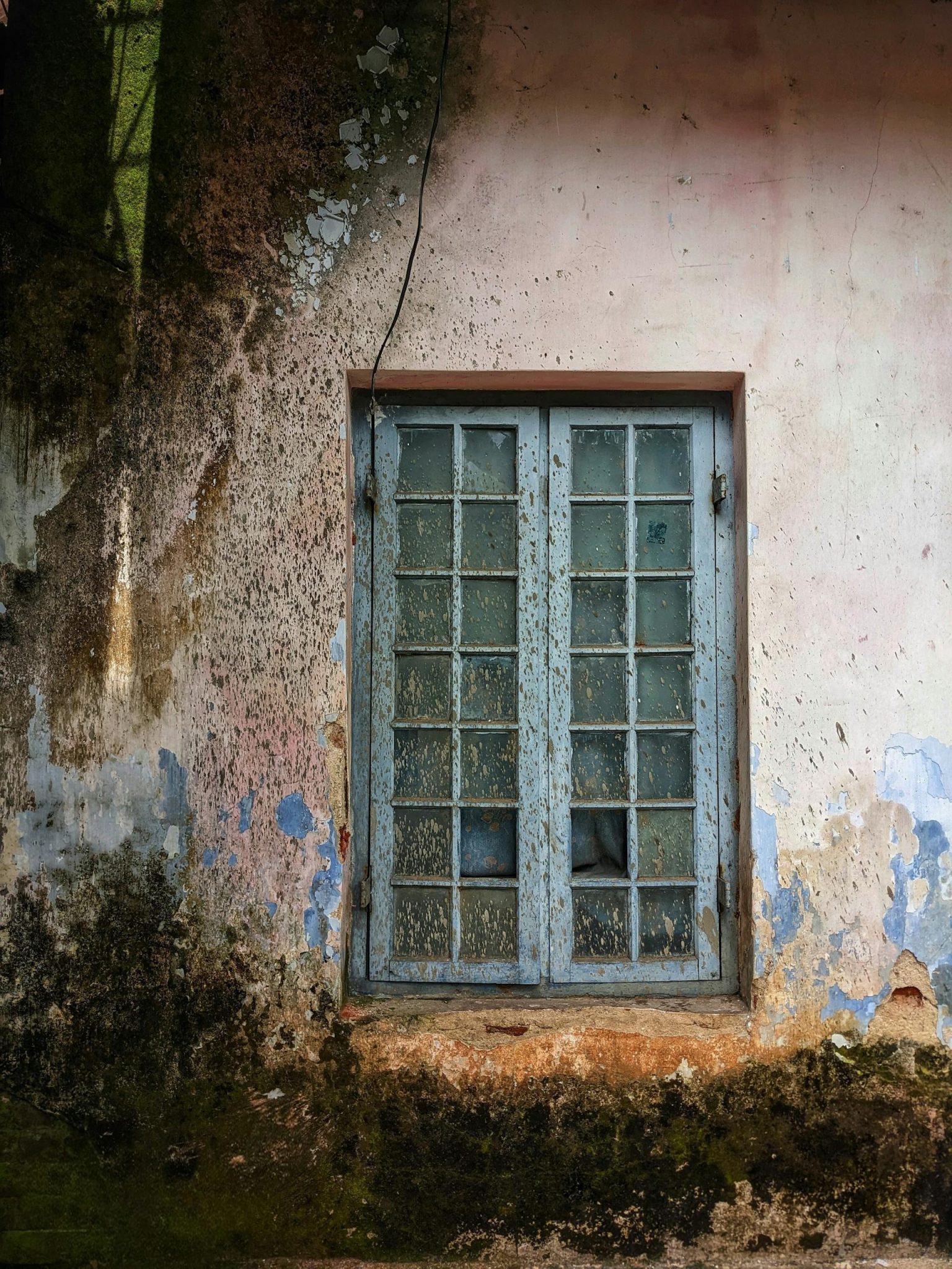 Fereastră veche pe un perete deteriorat.